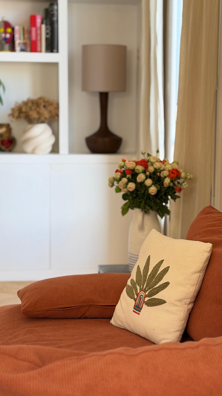Canapé en velours côtelé terracotta, coussin brodé et bouquet de roses dans un salon lumineux