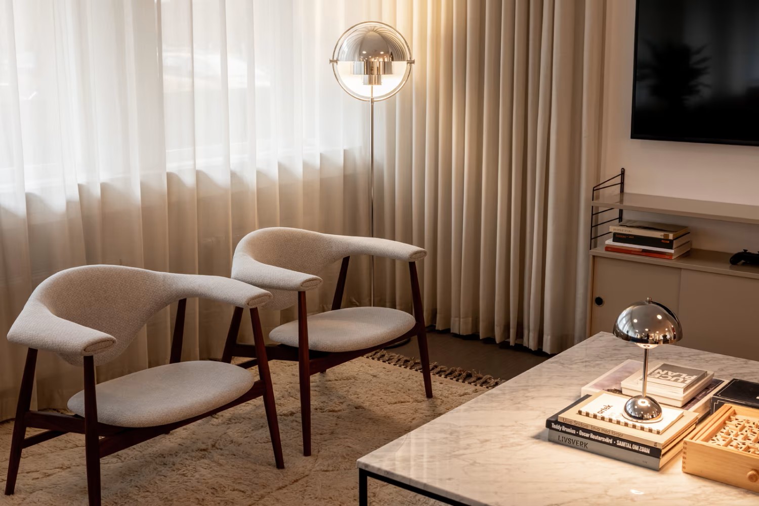 Deux fauteuils en tissu clair, lampadaire chromé et table basse en marbre dans un salon feutré