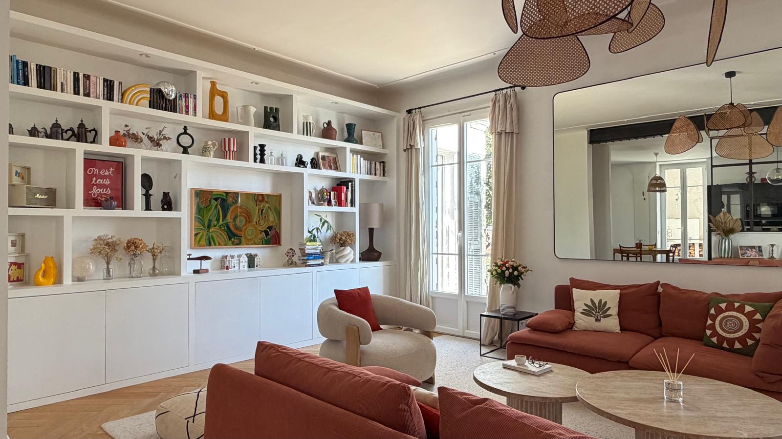 Séjour ouvert avec bibliothèque blanche sur-mesure, canapé en velours côtelé terracotta et grand miroir